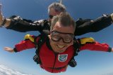 Tandem student with a red jumpsuit smiles with flapping cheeks during freefall