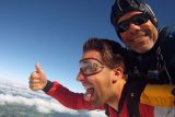 Tandem student sticks his thumb up and sticks his tongue out while his instructor smiles during freefall