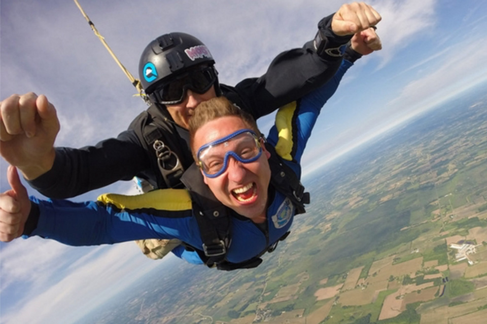 Tandem skydiver gives a thumbs up and an open excited mouth