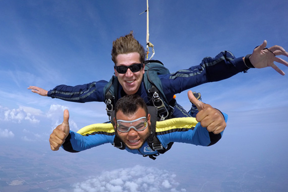 Male tandem skydiving pair give thumbs up.