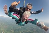 Older skydiver with grey hair in freefall with her tandem instructor