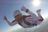 Skydiver in a white jumpsuit flies belly to earth giving double thumbs ups