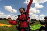 Girl in a red jumpsuit fist pumps in the air after landing from a skydive