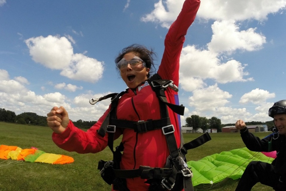Girl in a red jumpsuit fist pumps in the air after landing from a skydive