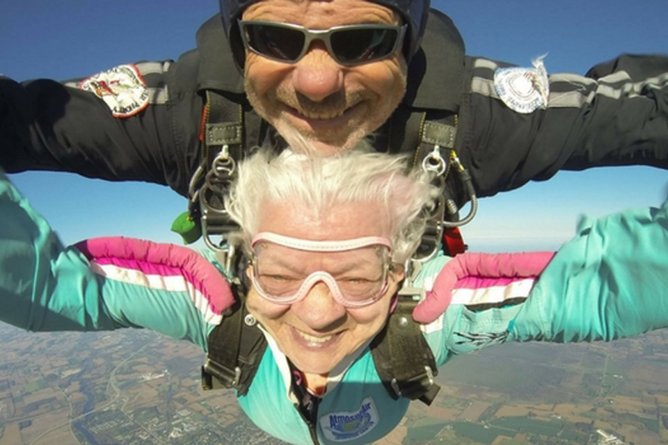 Older skydiver in freefall smiles with her tandem instructor