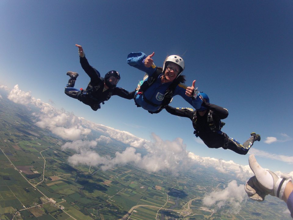 An AFF skydiving student gives two thumbs up during free fall while being assisted by two skydiving instructors. 