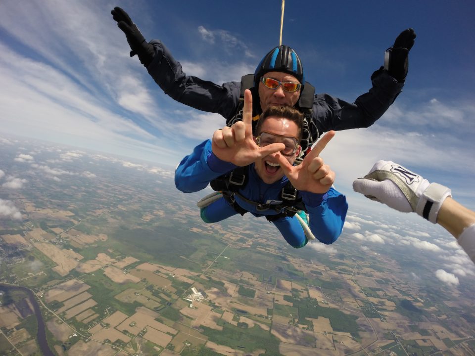 A University of Wisconsin graduate skydiving and giving a hand sign after getting a graduation gift certificate to Wisconsin Skydiving Center near Milwaukee