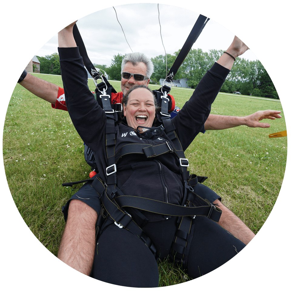 Tandem student smiles and raises her arms in celebration after landing from a skydive