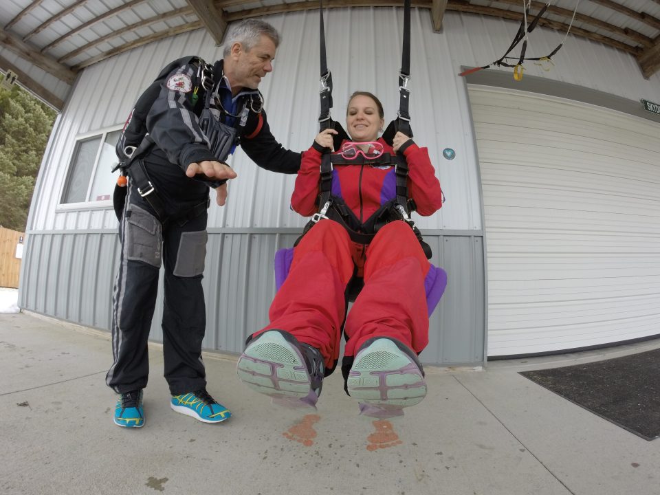 A tandem student lifts their legs in the hanging harness while training for skydiving safety