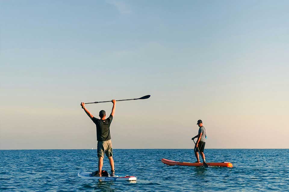 two people paddle boarding, one with his paddle over his head