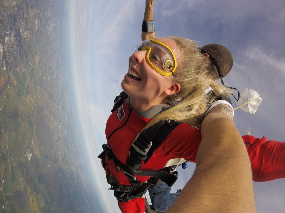 a young lady smiles during the free fall of her tandem skydive