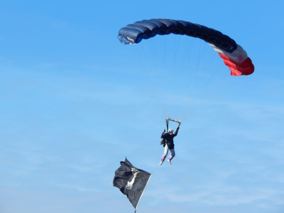 Jon Morgan flies under his parachute with an MIA flag trailing behind him.