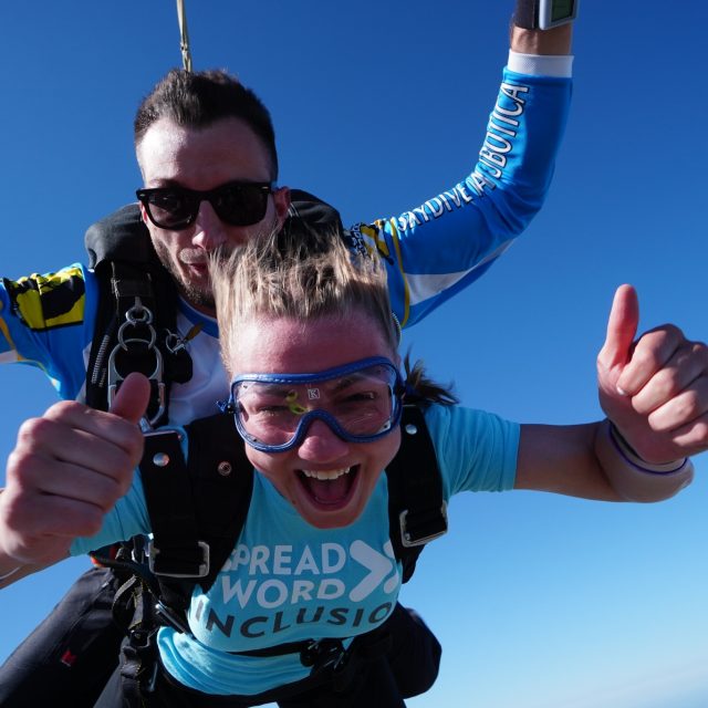 A woman giving thumbs up during tandem freefall after her first skydive at Wisconsin Skydiving Center