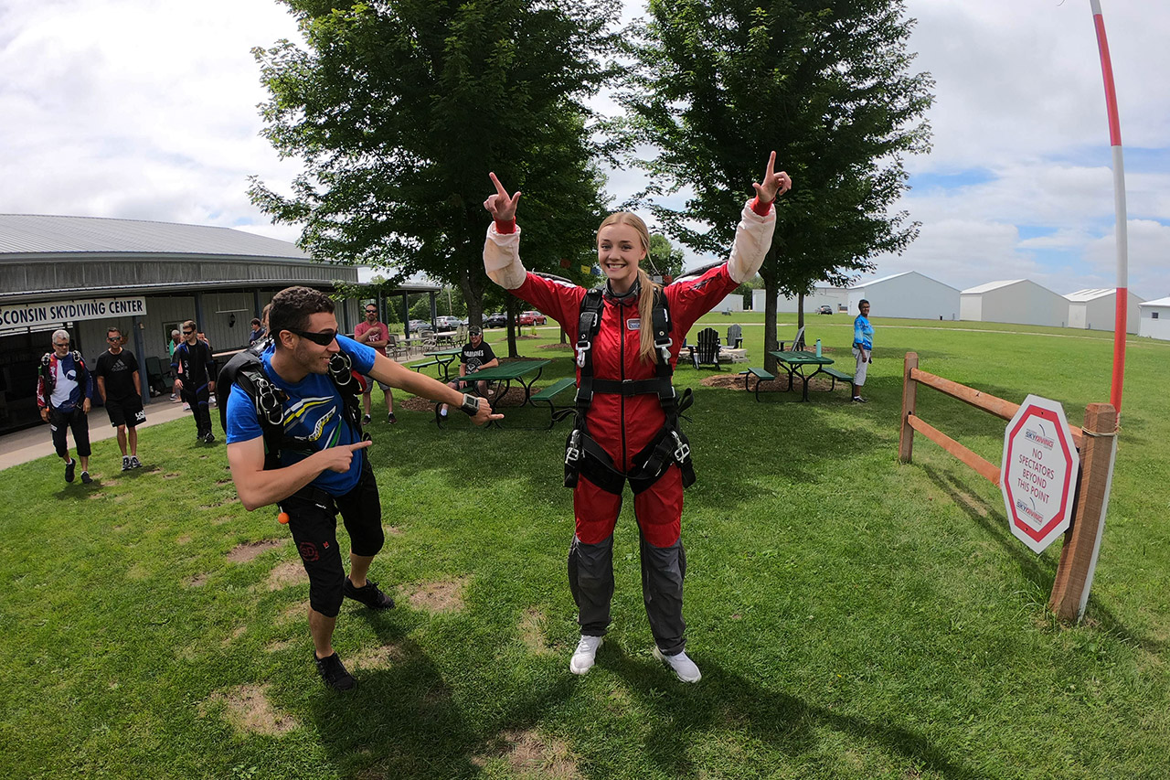 Female tandem student points two fingers in the air with a red jumpsuit and tandem skydiving harness