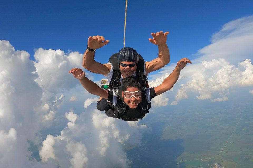 Male tandem skydiving pair with arms extended during freefall