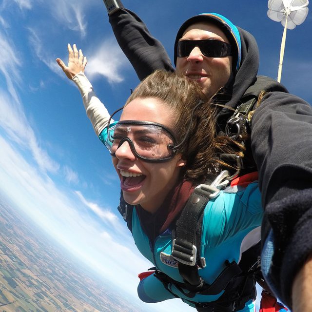 Female tandem skydiver smiles and extends her arms with her instructor under canopy