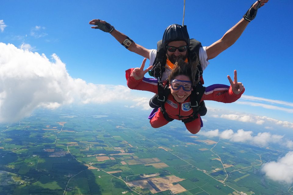 Tandem skydiver gives two peace signs in freefall with her instructor over Jefferson, WI