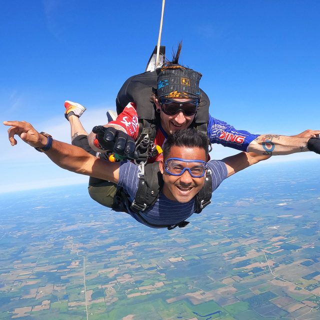 Male tandem student and his instructor with arms extended and smiling in freefall
