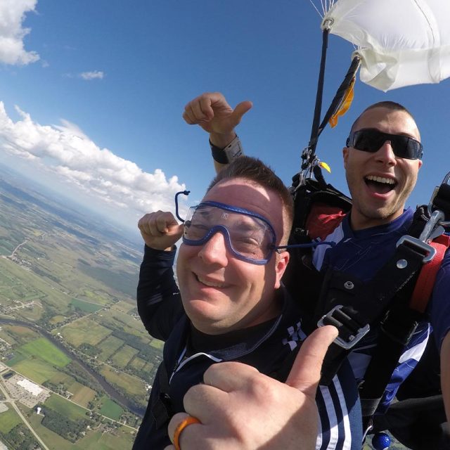 Male tandem skydiving pair give a thumbs up under canopy