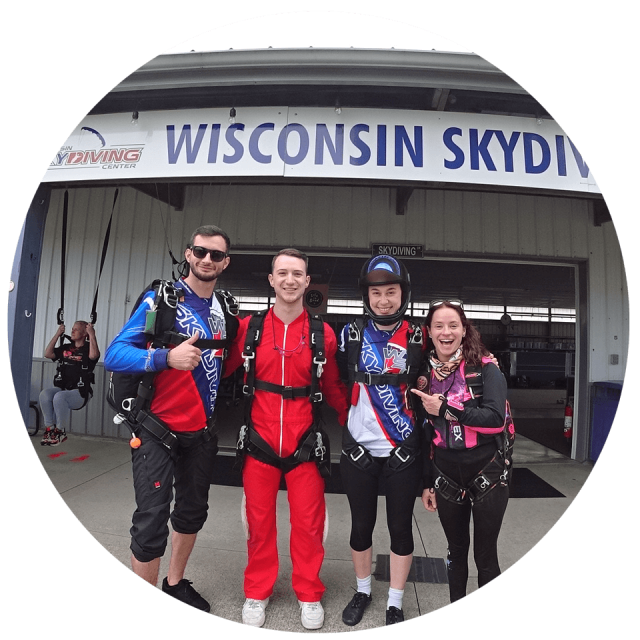 Tandem skydiver with his instructor and licensed skydivers post in front of the WSC sign