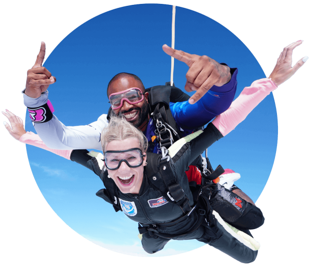 Blonde female tandem student in freefall with her instructor giving the shaka hand sign.