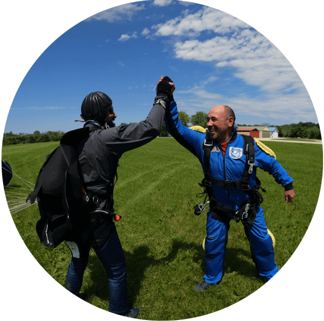 Male tandem student in a blue jumpsuit give his instructor a big high five following landing from their skydive.