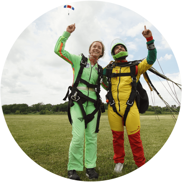 Tandem skydiver and her instructor point to the sky after landing