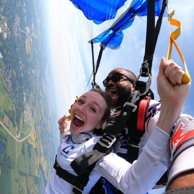 Tandem skydiving student and her instructor under canopy with mouths open
