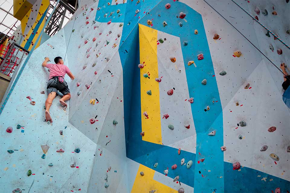 Man climbing indoor rock wall halfway up. 