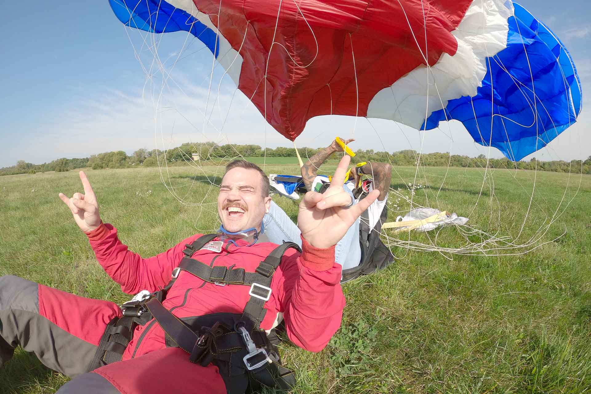 Male mustachioed tandem skydiver smiles open mouthed after landing from his jump