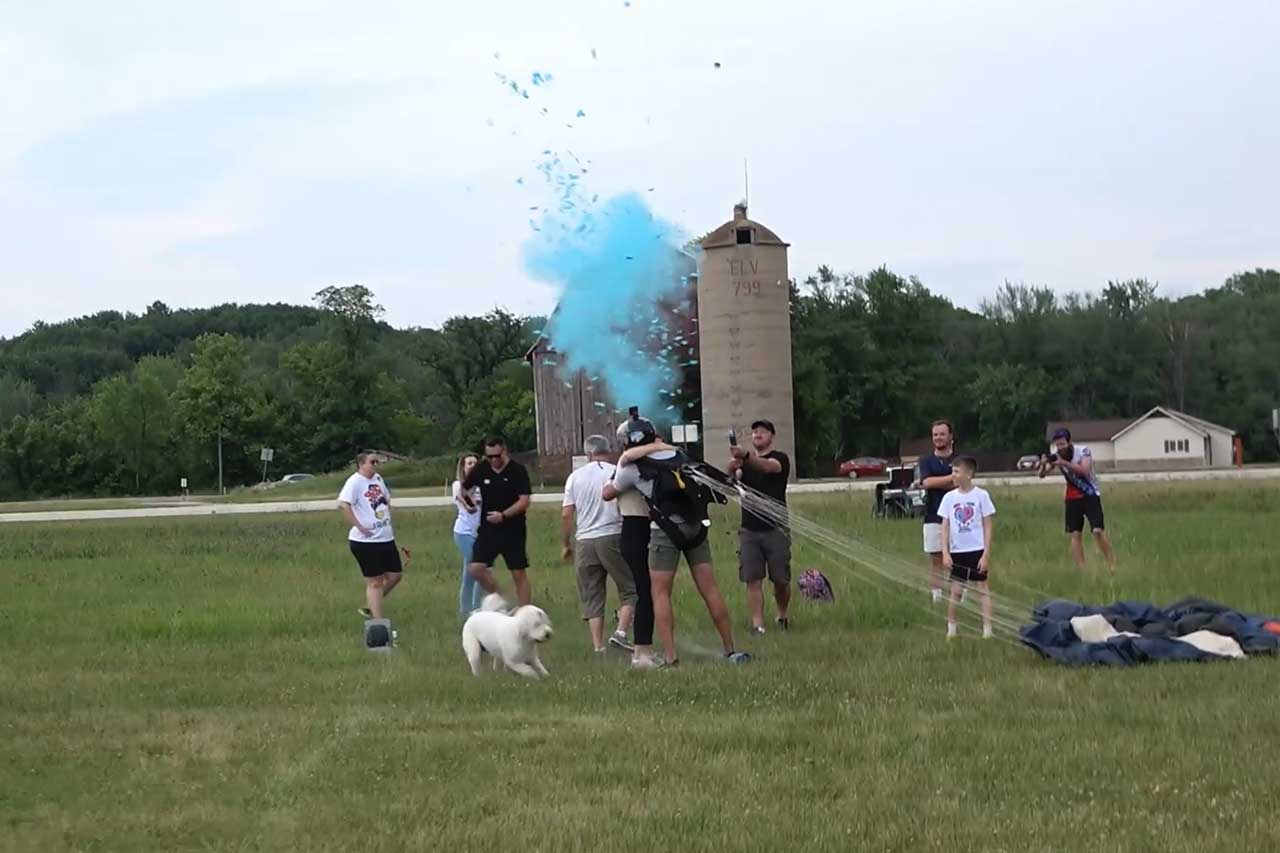 Family gathers on the ground after a skydiving gender reveal.